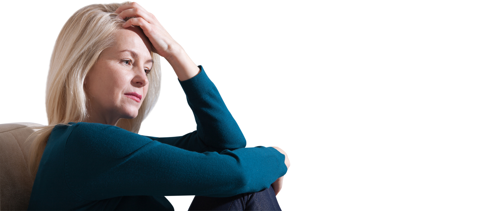 Woman suffering from stress or a headache grimacing in pain. Sad depressed woman at home sitting on the couch, looking down and touching her forehead, loneliness and pain concept